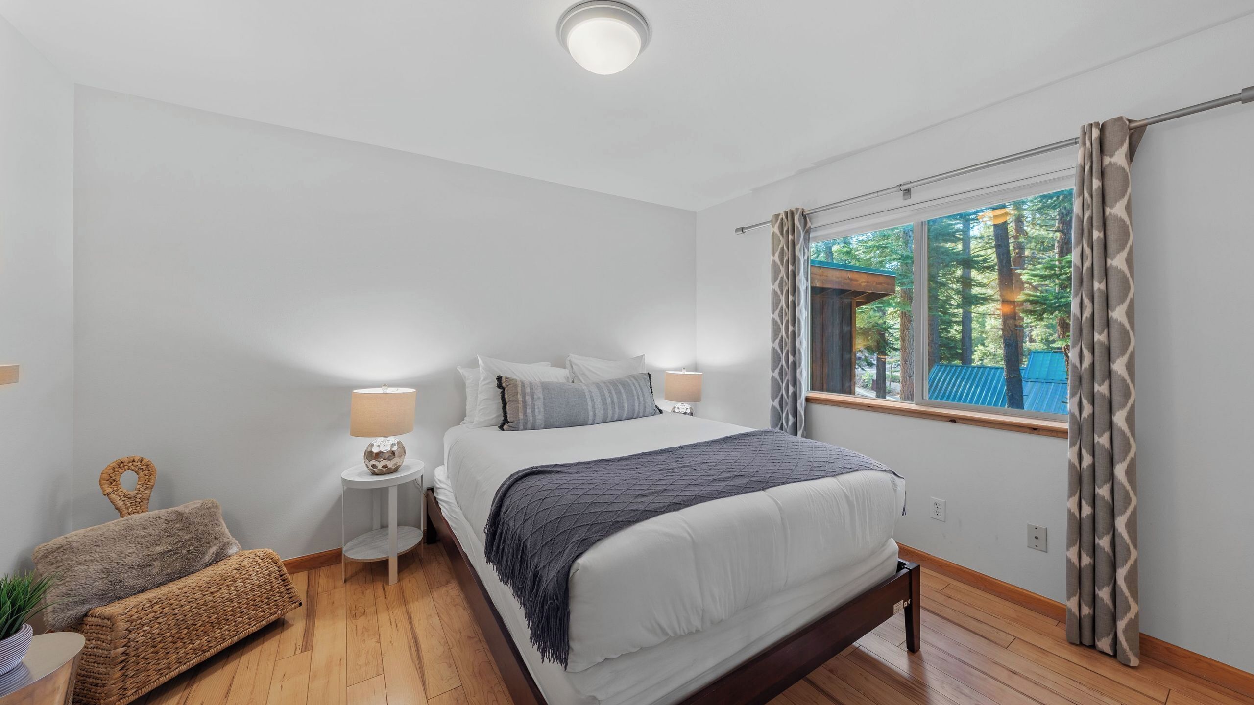 A bedroom with a bed, two bedside tables, a lamp, a chair, and a window with curtains.