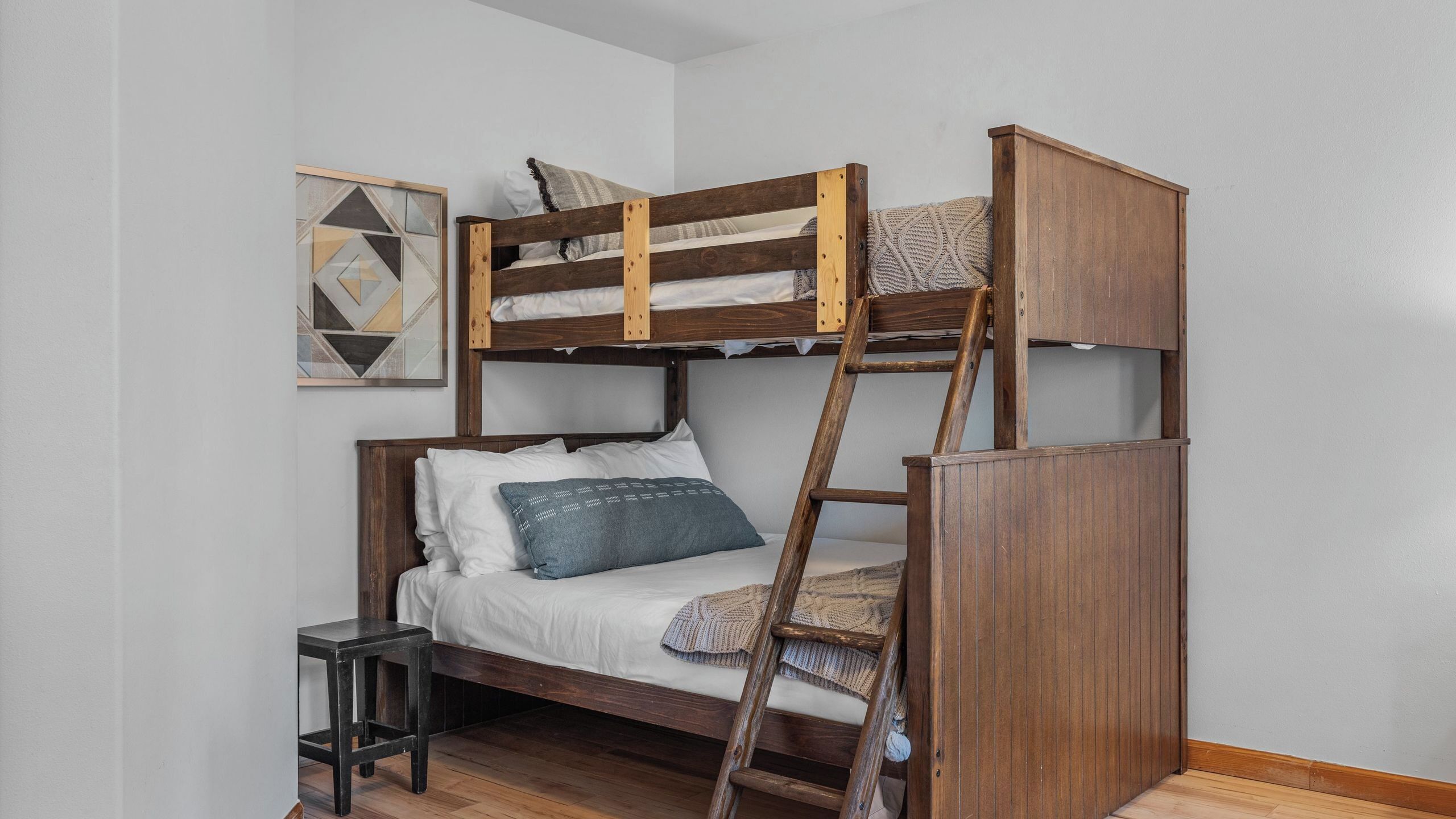 A bunk bed with a ladder, white bedding, and a small side table.