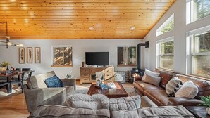 Una sala de estar acogedora con techo de madera, chimenea, televisor y un ventanal grande.