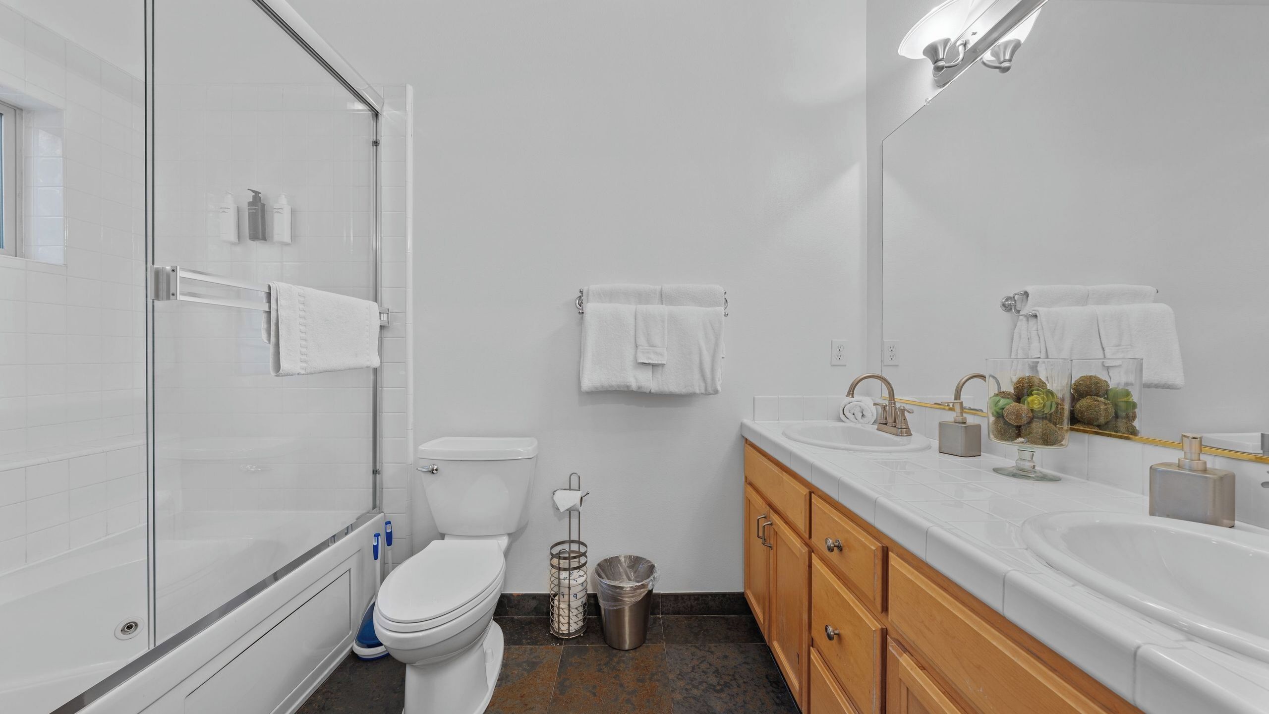 A modern bathroom with a glass shower enclosure, a toilet, a sink with a mirror, and wooden cabinets.