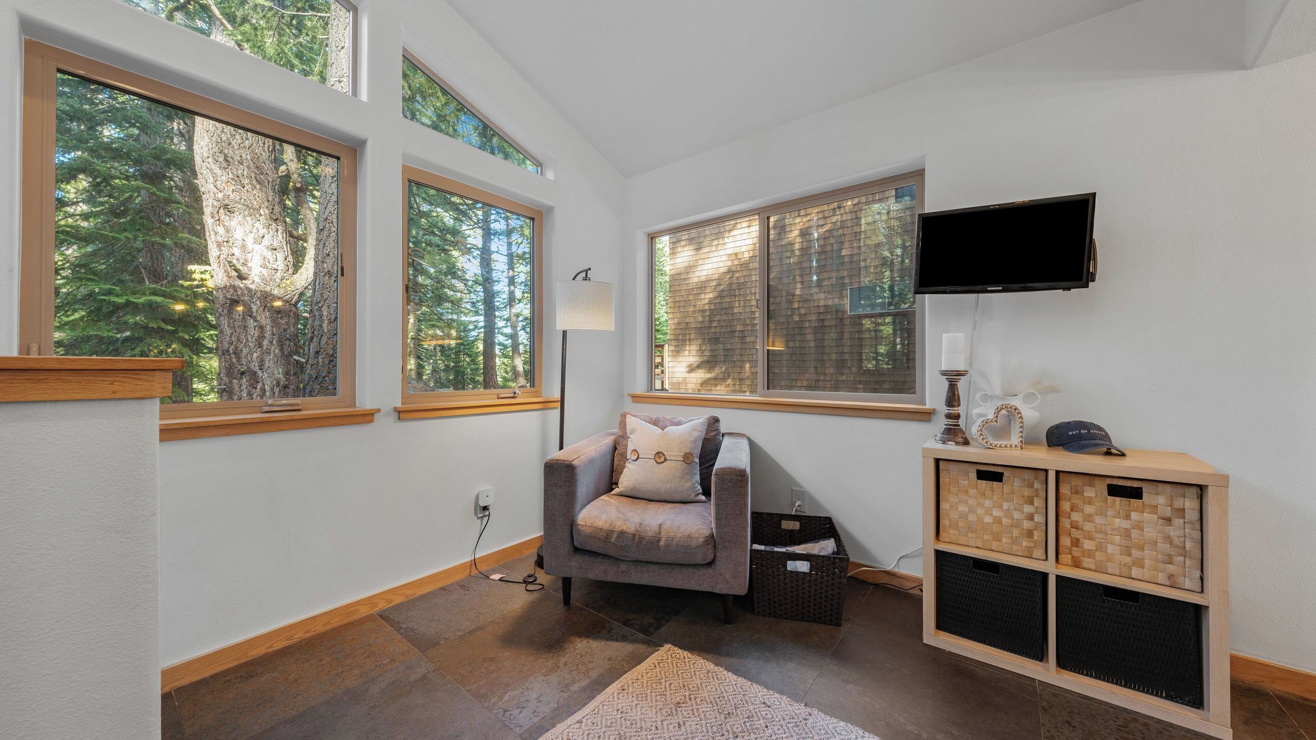 Una habitación acogedora con amplias ventanas, un sillón cómodo, un televisor y un armario de madera.
