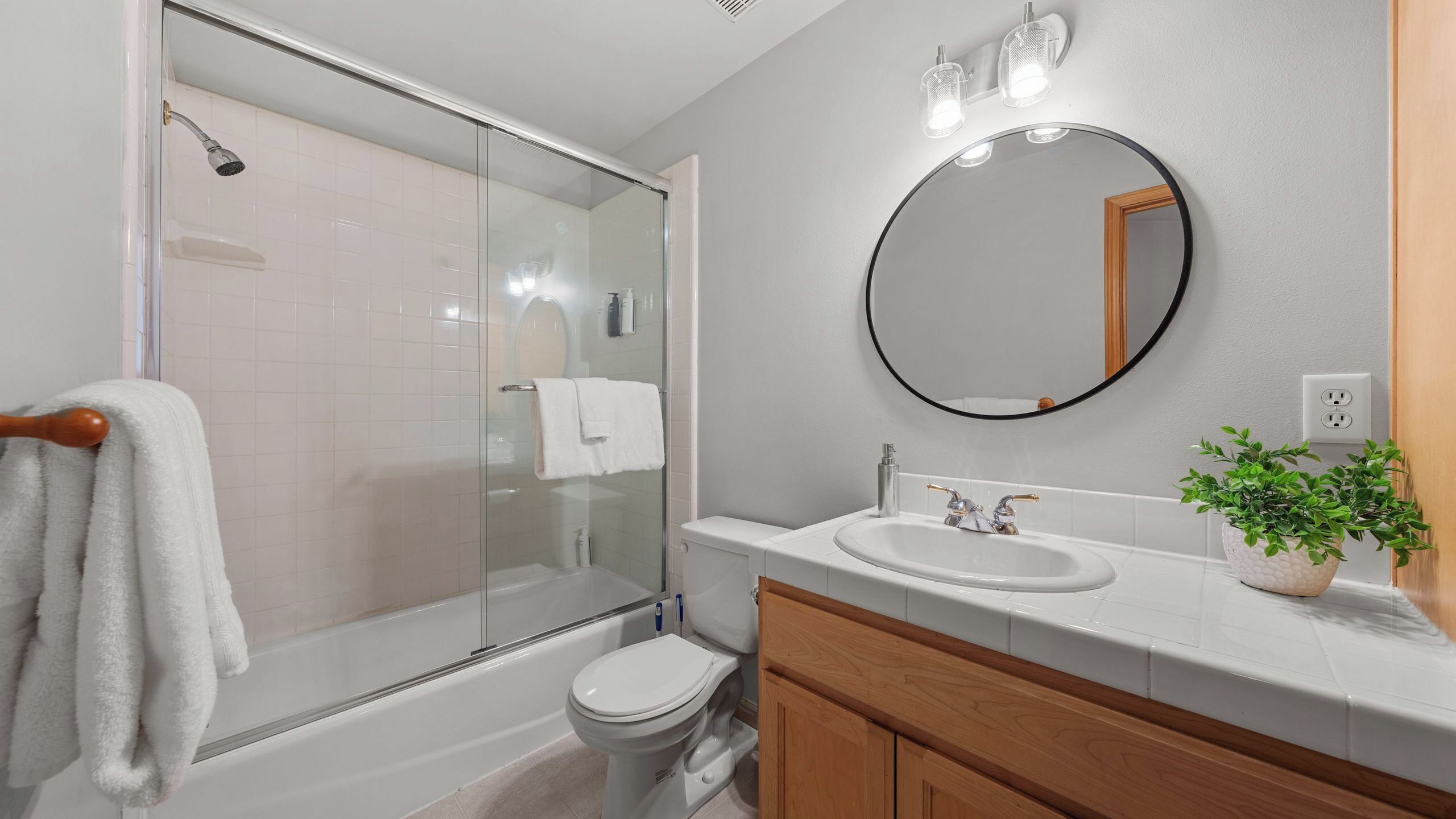 A modern bathroom with a glass-enclosed shower, a white toilet, a sink with a mirror, and a wooden vanity.