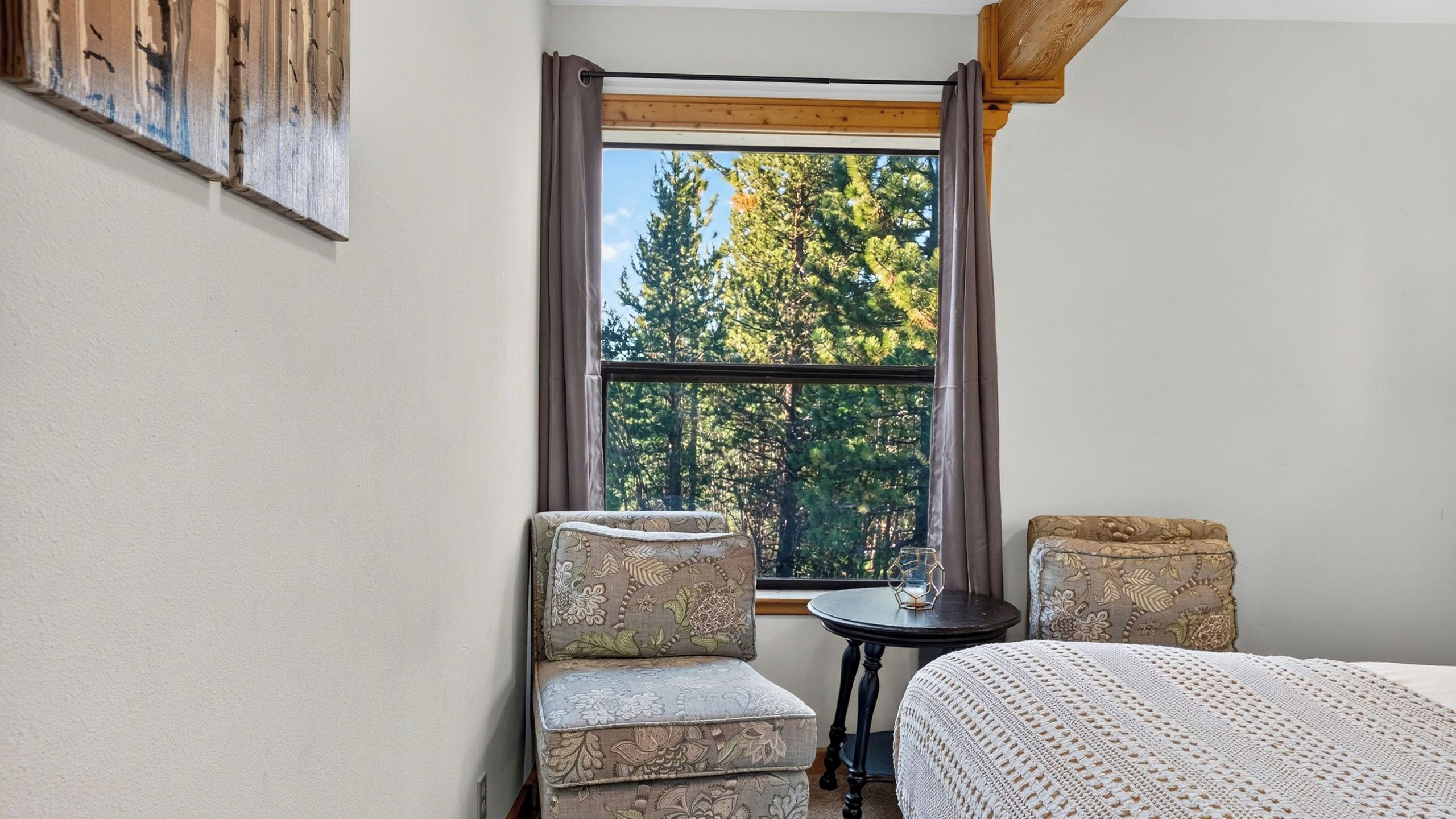 A room with a bed, two chairs, a small table, and a window with a view of trees.