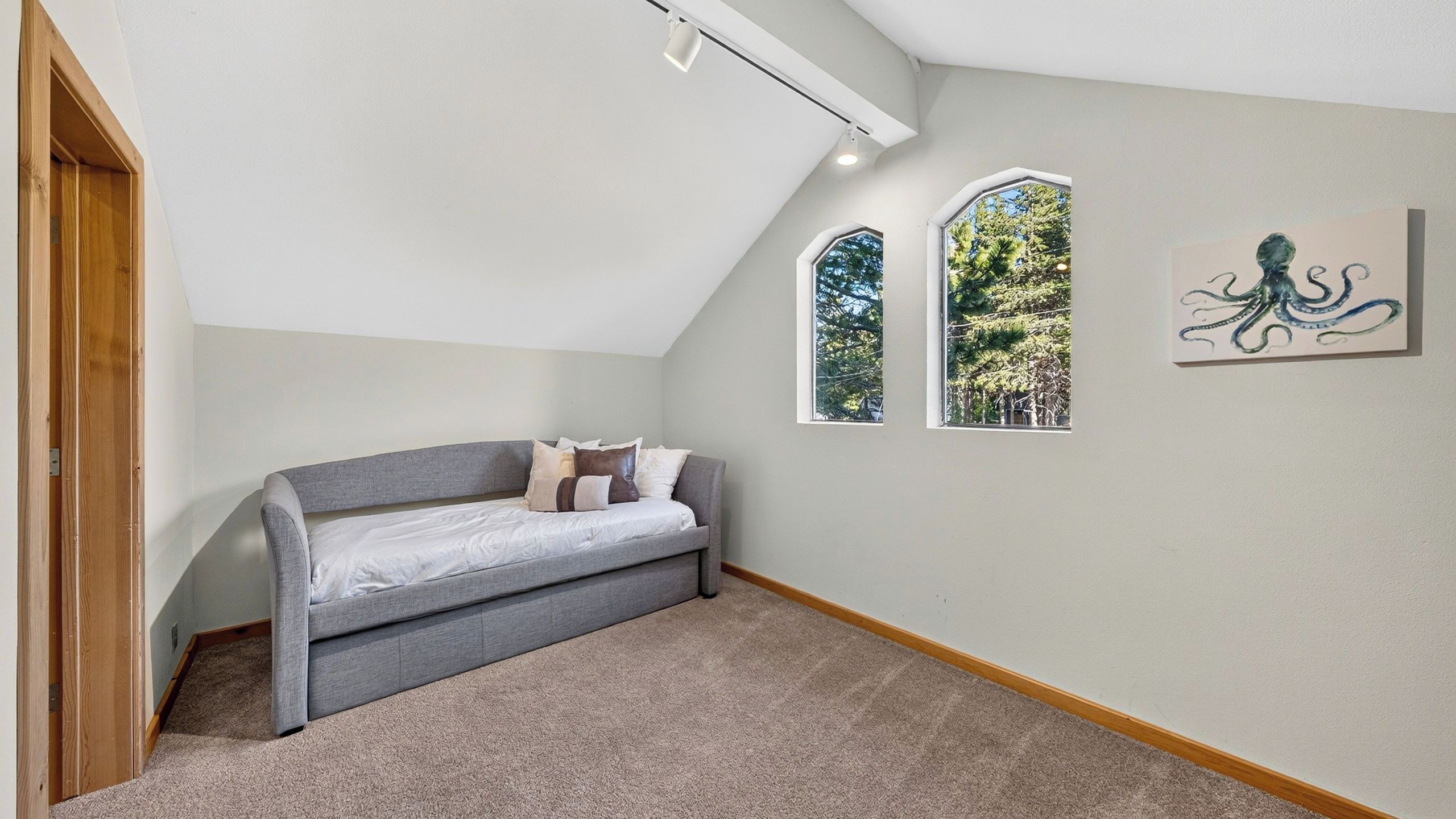 A room with a gray sofa, two arched windows, and a painting of an octopus on the wall.
