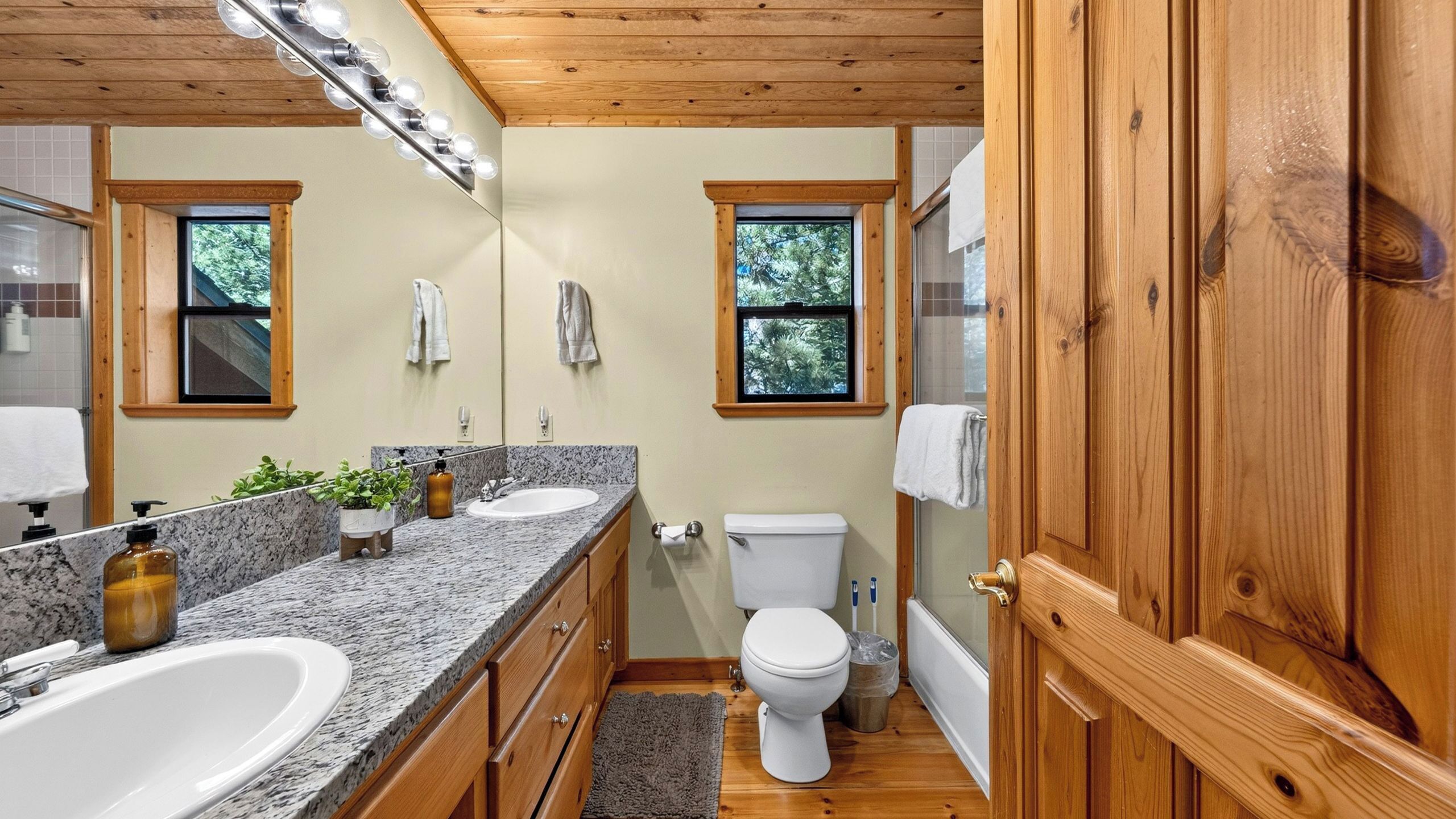 Un baño con lavamanos doble, inodoro y puerta de madera.