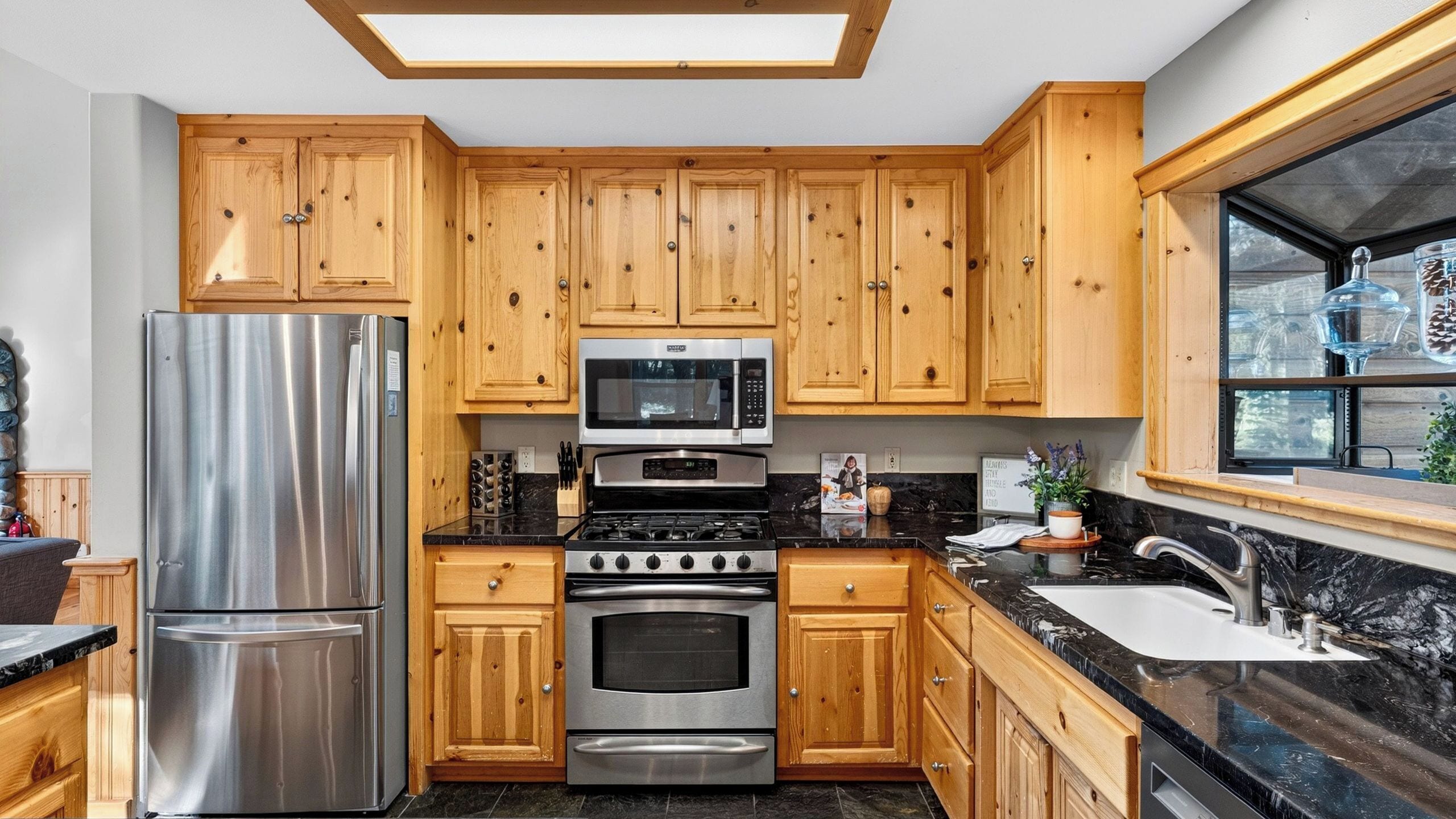A modern kitchen with wooden cabinets, stainless steel appliances, and a window with decorative items.