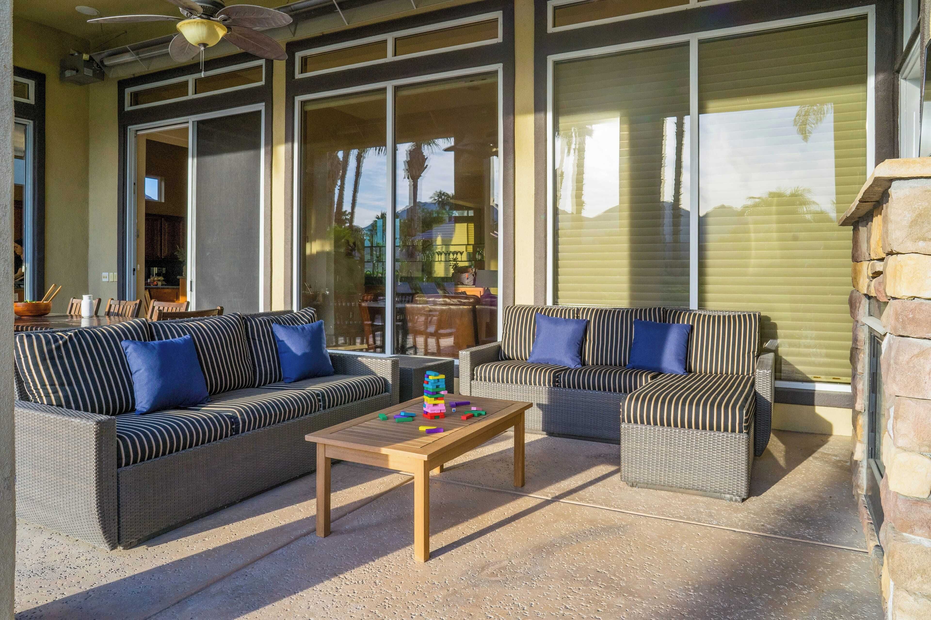 Un patio al aire libre con mobiliario de mimbre, una mesa de centro de madera y ventanas amplias.