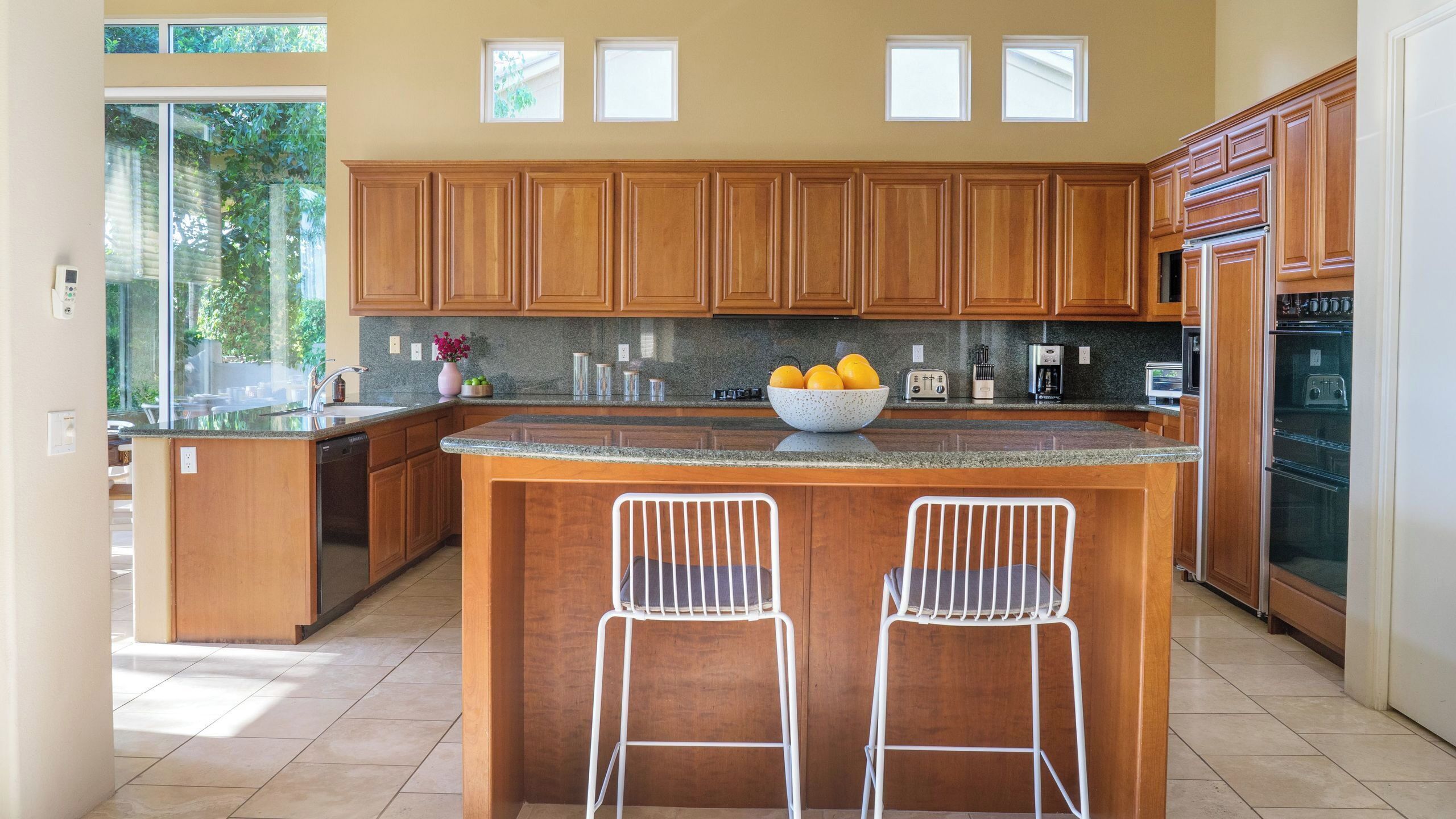 A modern kitchen with wooden cabinets, a granite countertop, a central island with two bar stools, and built-in appliances.
