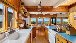 A modern kitchen with wooden cabinetry, a large island, and a view of the ocean. - The Pilot House by Avantstay Stunning Home Right On Arch Cape Beach! (Arch Cape)