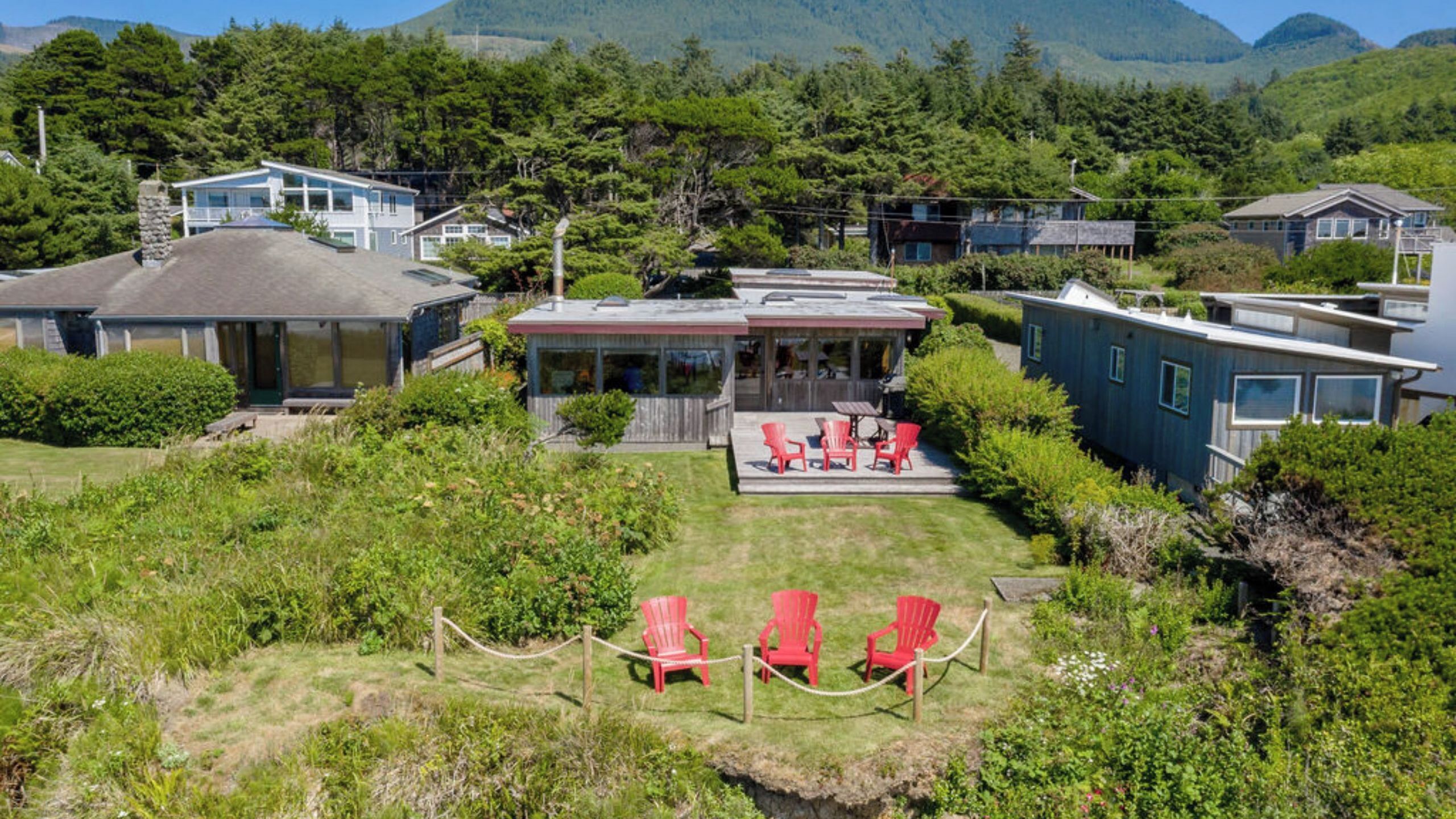 Een landgoed aan de kust met een overdekt terras, rode stoelen en uitzicht op zee en bergen.