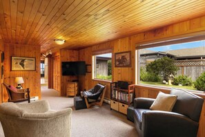 A cozy wooden interior with a sofa, armchairs, a TV, and a bookshelf. - The Pilot House by Avantstay Stunning Home Right On Arch Cape Beach! (Arch Cape)