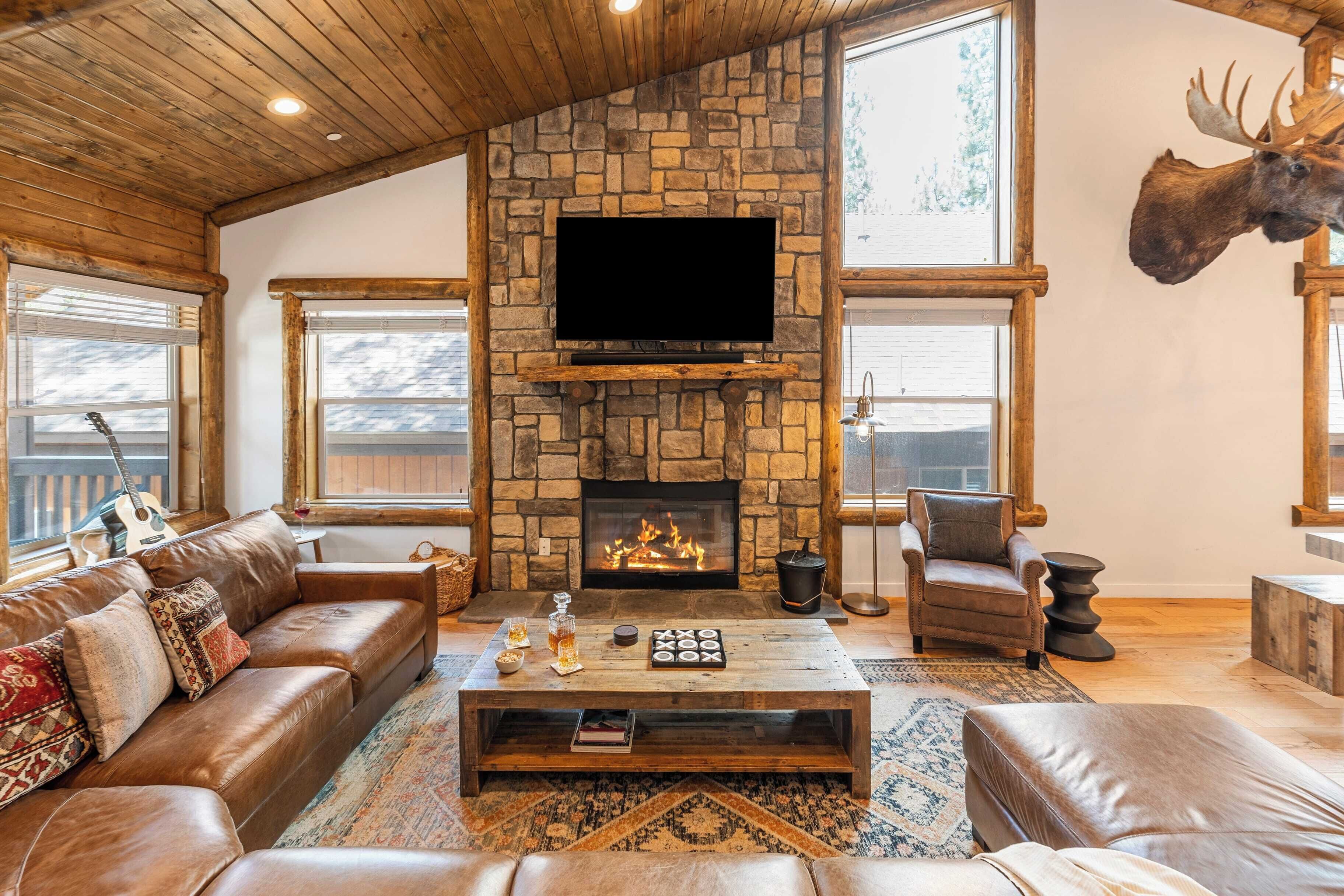 A cozy living room with a stone fireplace, leather sofas, and a mounted moose head.