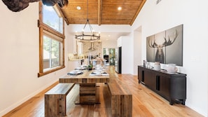 Une cuisine spacieuse avec un plancher en bois, une grande table à manger pouvant accueillir six personnes, un lustre moderne et une décoration murale représentant une tête de cerf.