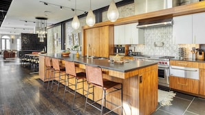 A modern kitchen with a large island, bar stools, stainless steel appliances, and pendant lighting.