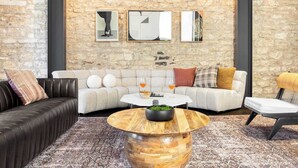 A modern living room with a stone wall, a black leather sofa, a white sofa, a round wooden coffee table, and a black chair.