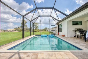 Una piscina exterior con cerramiento de vidrio, rodeada de un patio con mobiliario exterior.