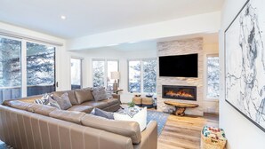 A modern living room with a leather sofa, a fireplace, and large windows. - Manitou Riverhouse 115 by Avantstay Spacious Condo in the Centre of Telluride (Telluride)
