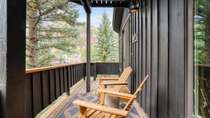 A wooden deck with two chairs and a rug, overlooking a forested area. - Manitou Riverhouse 115 by Avantstay Spacious Condo in the Centre of Telluride (Telluride)