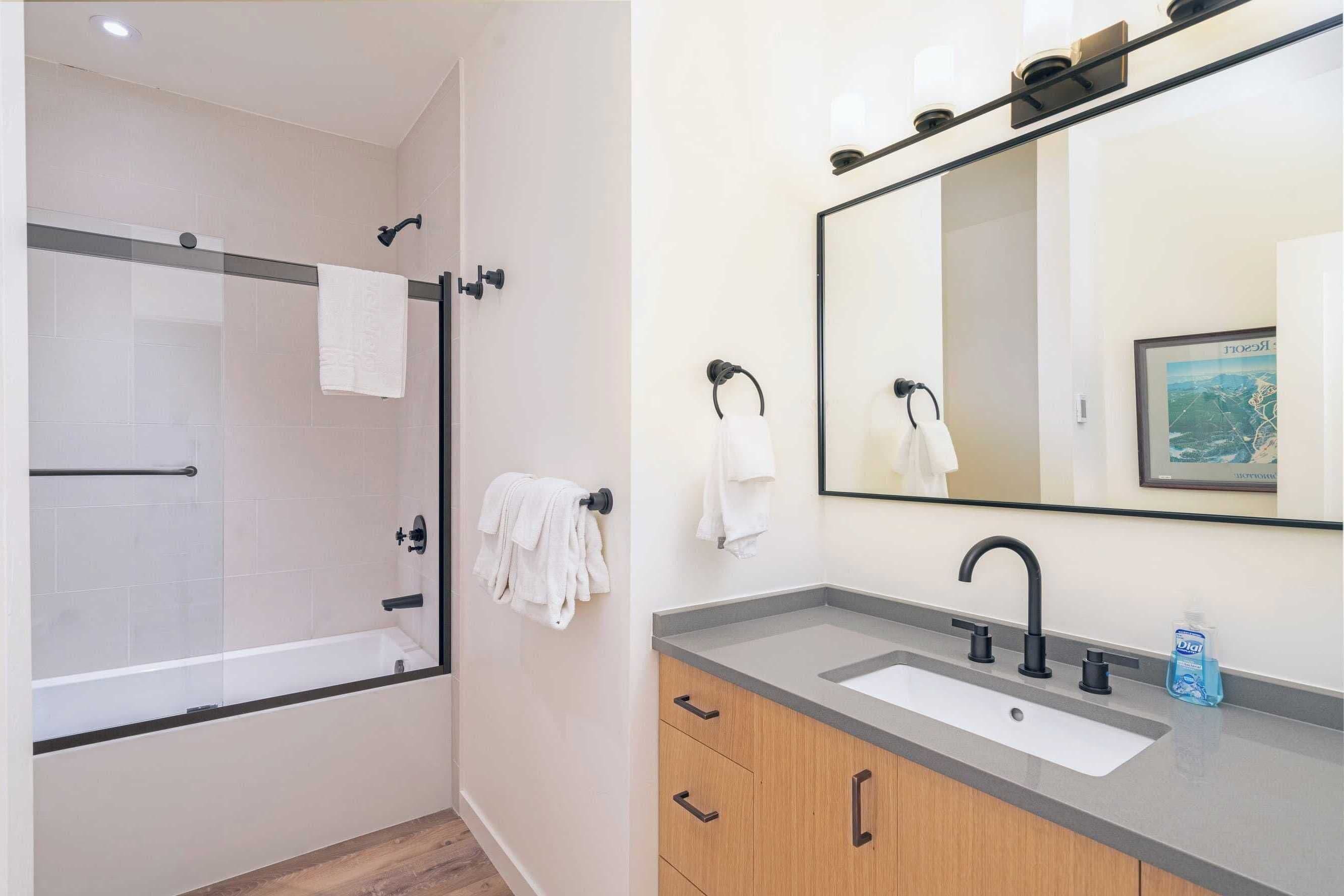 A modern bathroom with a glass-enclosed shower, a sink with a mirror, and wooden cabinets.