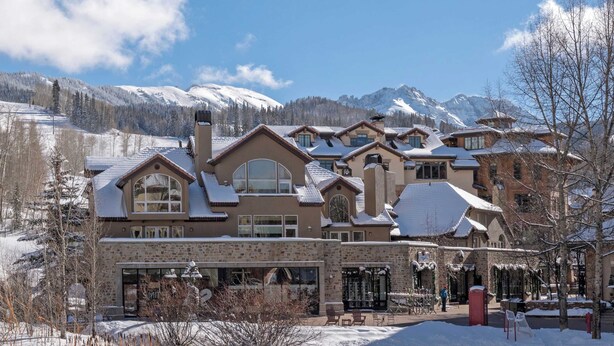 Un grand chalet à plusieurs étages, doté d’une façade en pierre, de nombreuses cheminées et de grandes fenêtres.