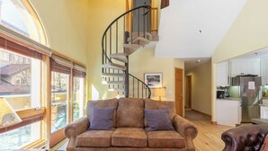 Un salon chaleureux avec un canapé marron, un fauteuil en cuir marron et un escalier en colimaçon menant à l’étage supérieur.