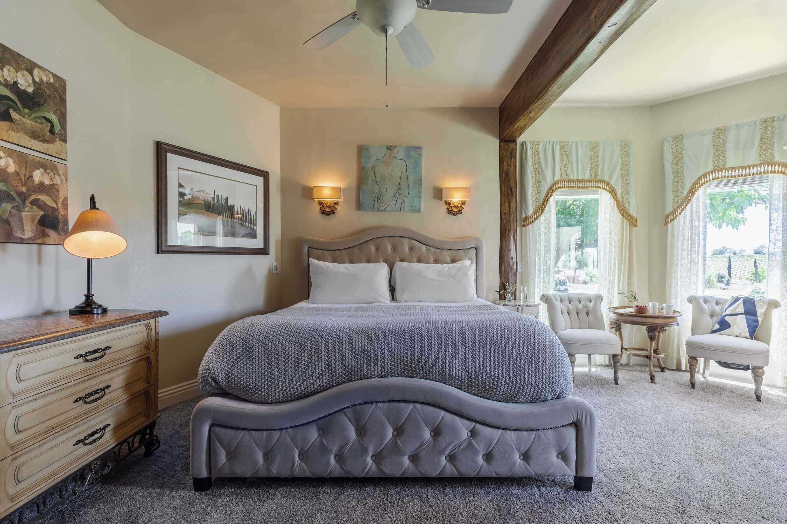 A bedroom with a large bed, a nightstand, a lamp, a chair, and a table with a tray.