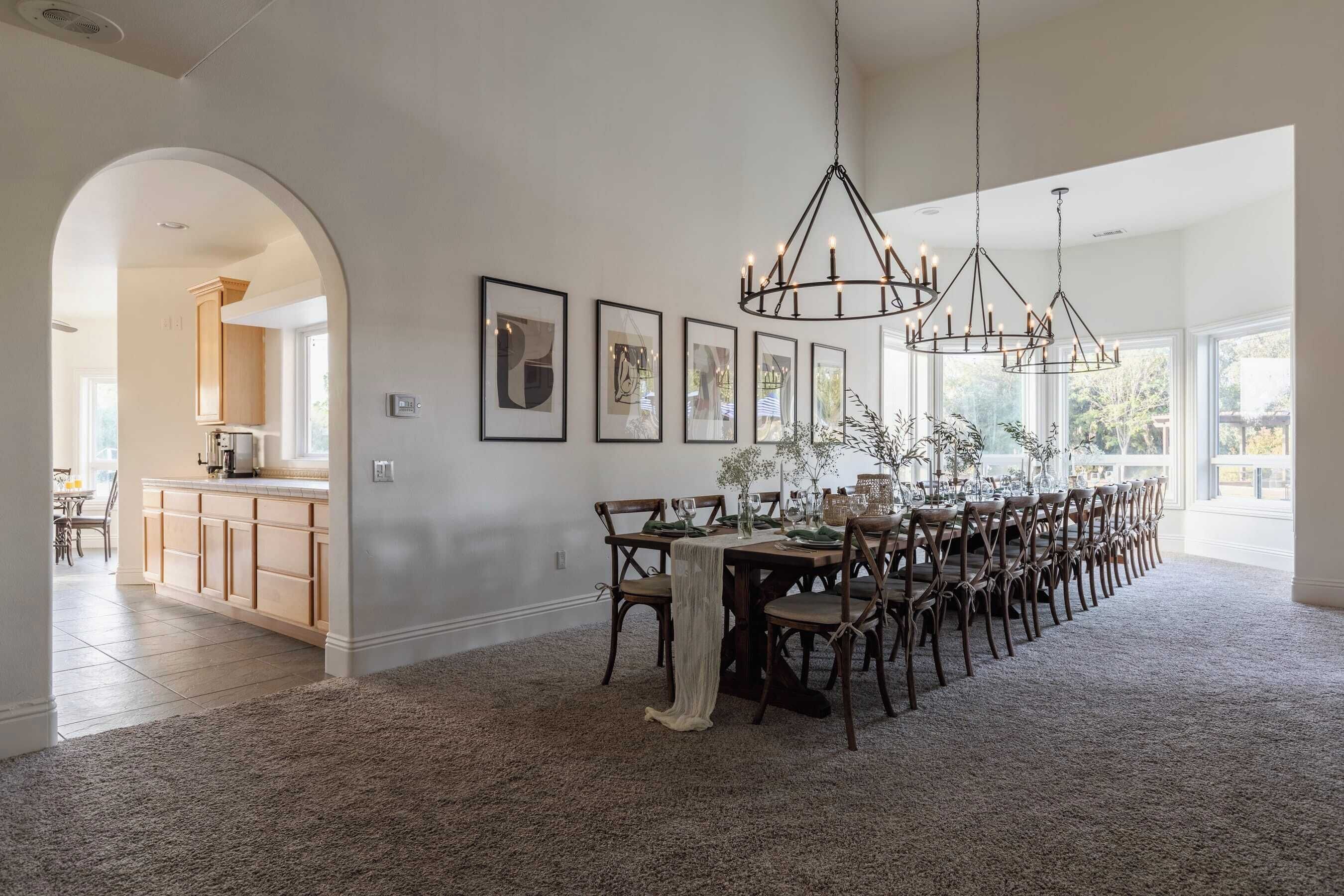 A spacious dining area with a long table set for multiple people, framed artwork on the walls, and a chandelier.