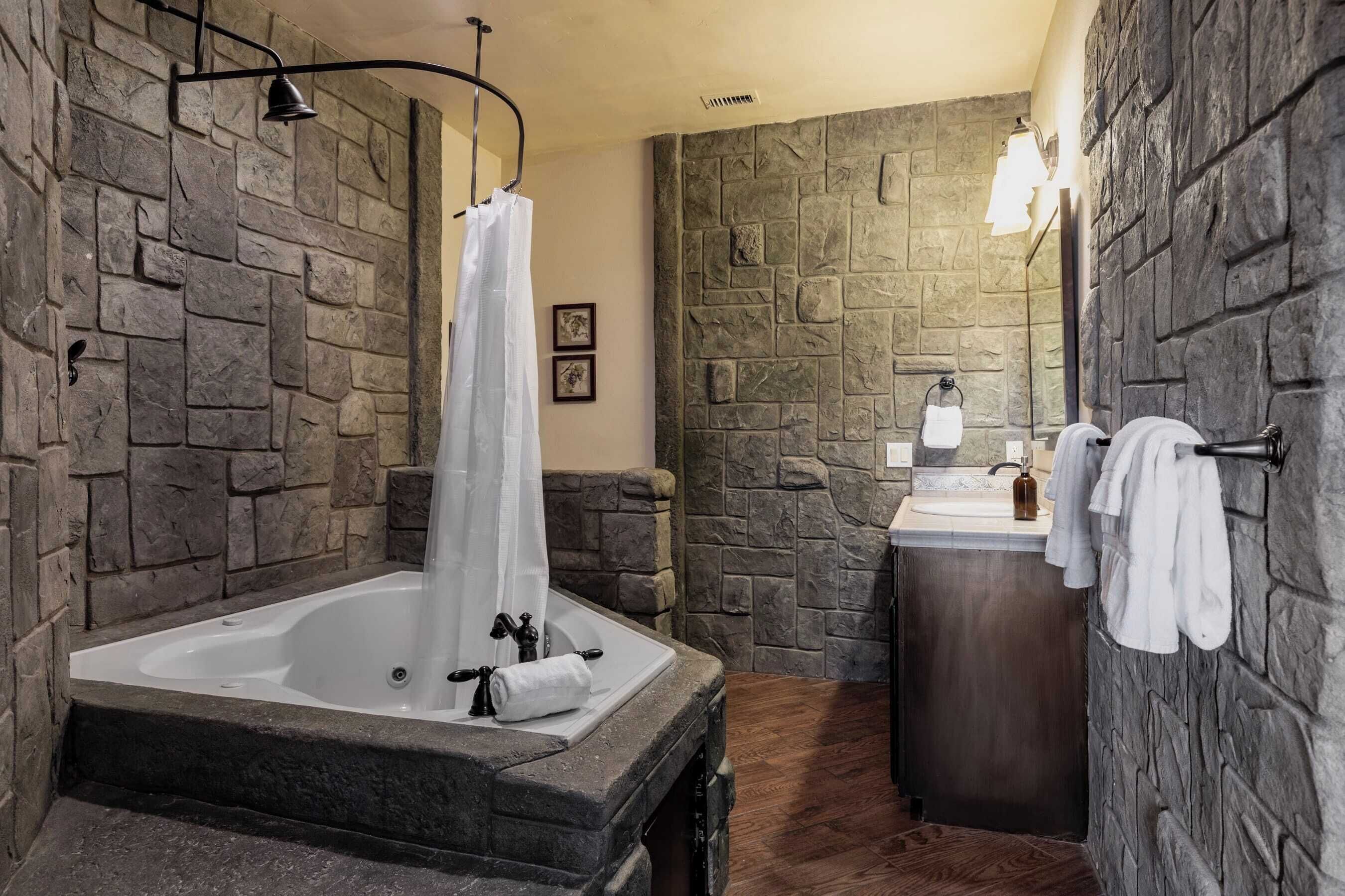 A bathroom with a stone wall, a bathtub, a sink, and a mirror.