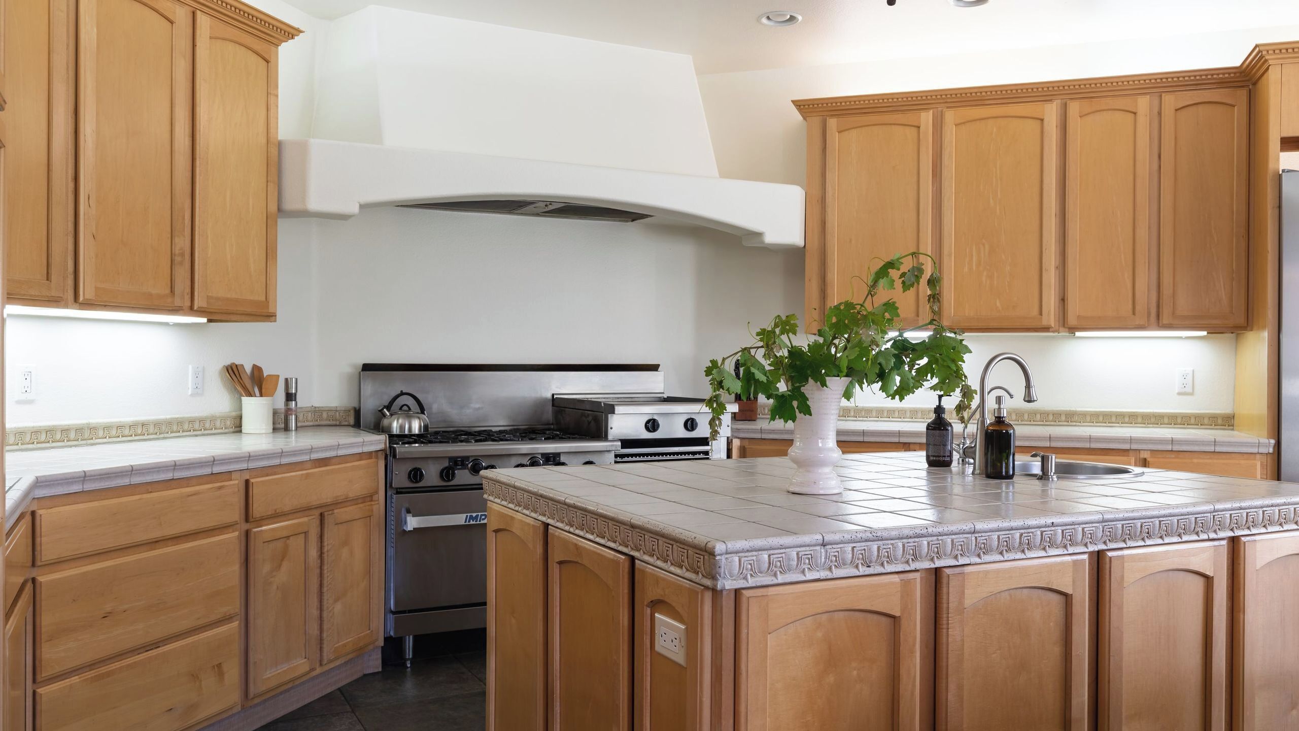 A kitchen with wooden cabinets, a stainless steel stove, a large island with a sink, and a potted plant.