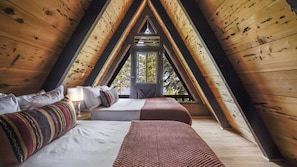 A triangular attic bedroom with wooden beams, a bed, a window, and a view of trees. - Horizon by Avantstay Stunning A-frame Cabin w/ Hot Tub, Billiards, Lake Views (Tahoe City)
