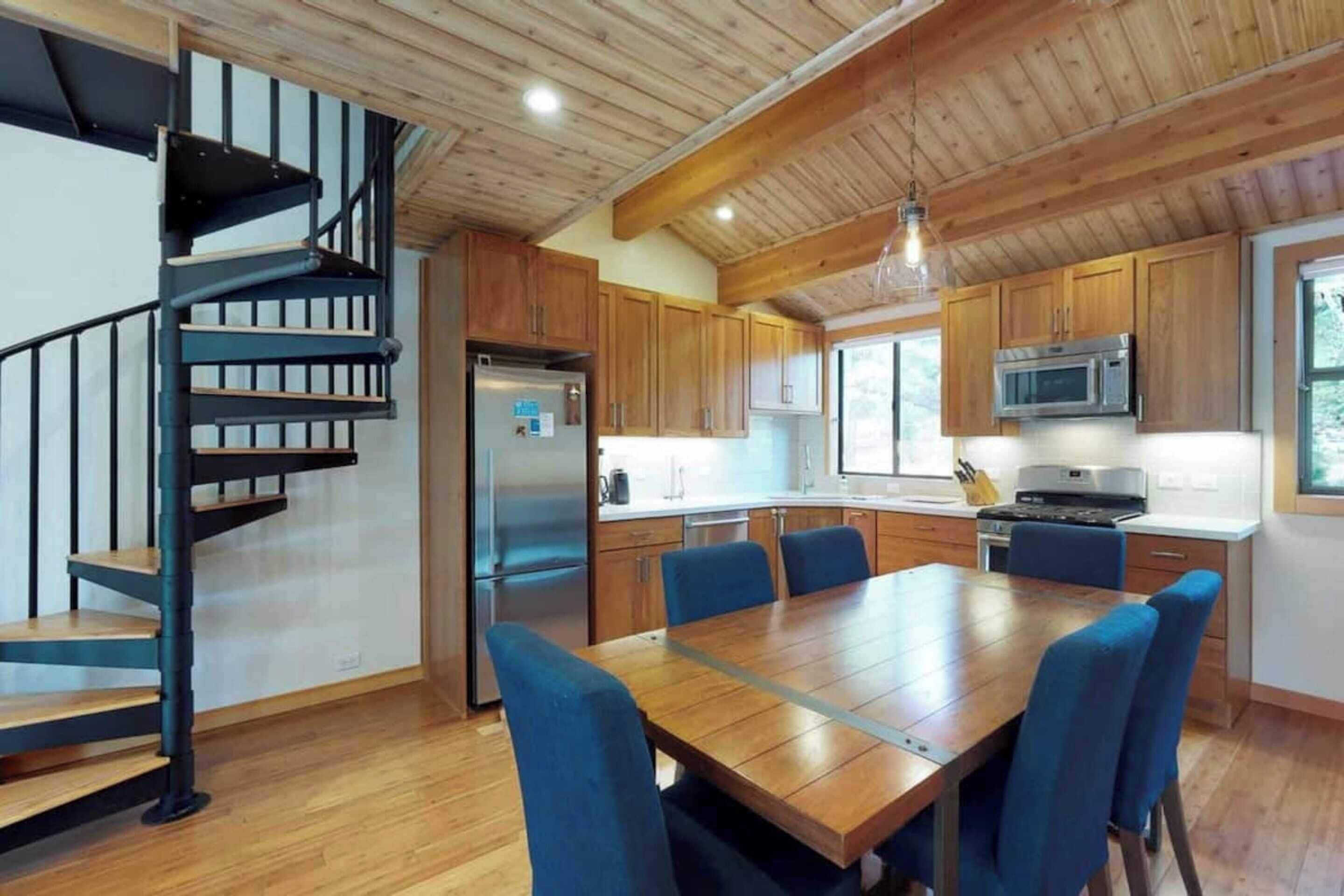 Een moderne keuken met houten kastjes, een roestvrijstalen koelkast, een magnetron en een eethoek met blauwe stoelen.