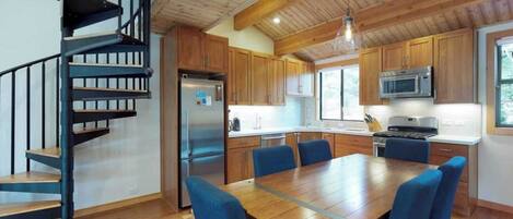 Een moderne keuken met houten kastjes, een roestvrijstalen koelkast, een magnetron en een eethoek met blauwe stoelen.