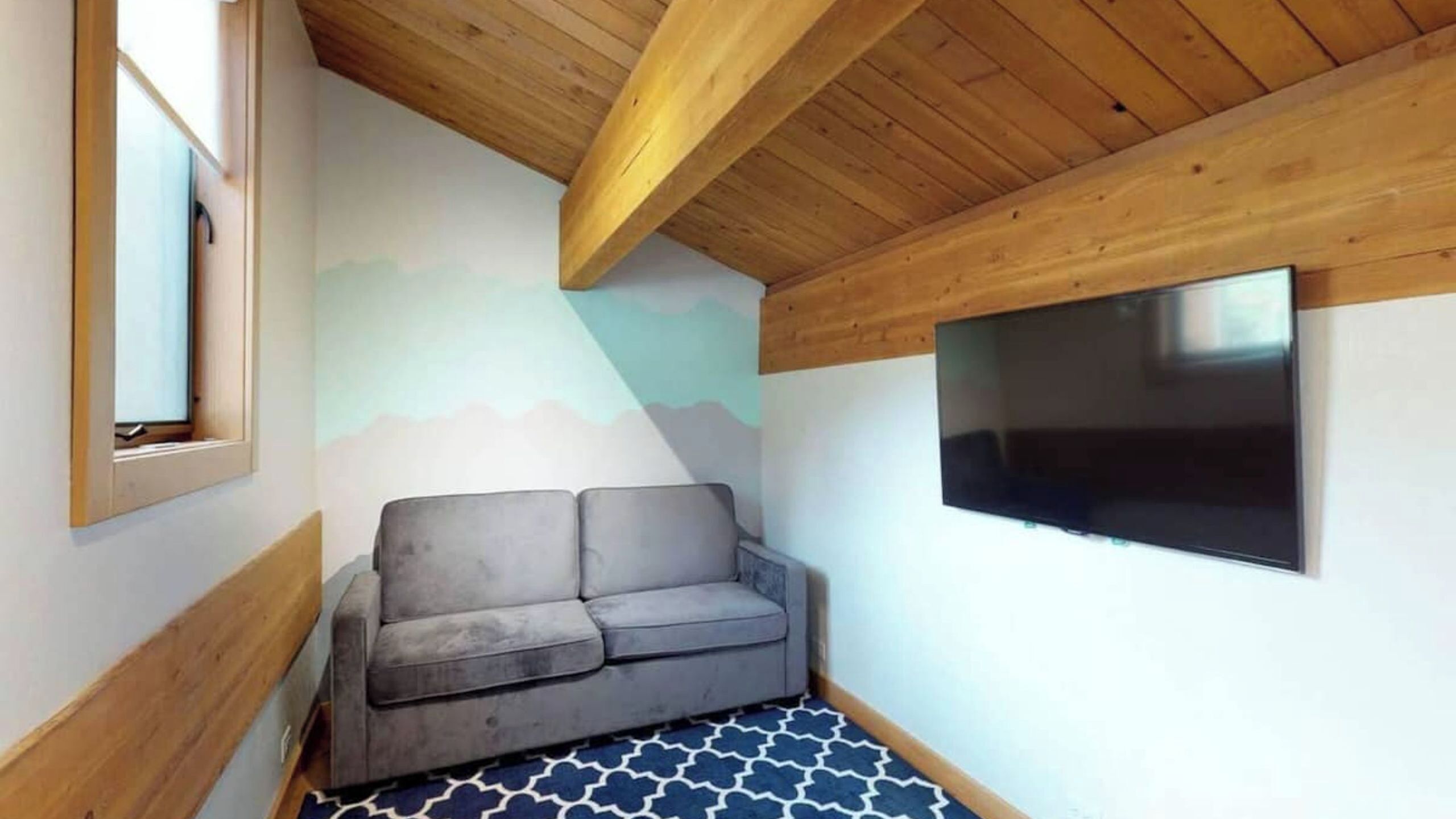 A room with a grey sofa, a mounted TV, and a patterned floor.