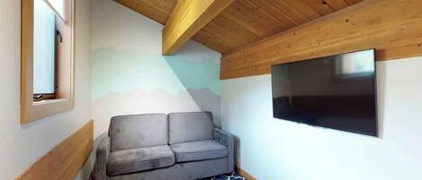 A room with a grey sofa, a mounted TV, and a patterned floor.