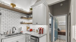 Una cocina compacta con armarios blancos, encimera de granito y lavavajillas integrado.