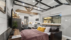 Un espacio habitable compacto con kitchenette, una cama con manta marrón, sofá de cuero y un ventanal que ofrece vistas al exterior.