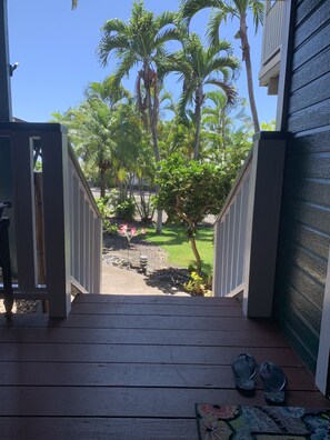 Una terraza de madera que da a un jardín con palmeras y una pequeña fuente.