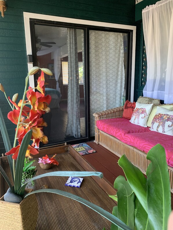 Una habitación con puerta de vidrio corredera, cama con ropa de cama estampada y planta en maceta con flores rojas.
