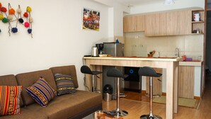 Ein kompakter Wohnbereich mit Küchenzeile, einem braunen Sofa mit gemusterten Kissen und einer Kaffeemaschine.