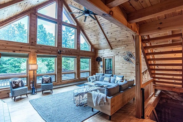 A spacious log cabin interior with a large sofa, two armchairs, and a dining table.
