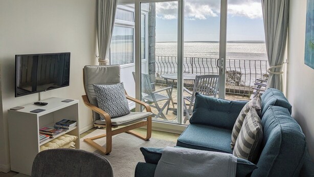 Un salon avec un téléviseur, une bibliothèque, un fauteuil, un canapé et une vue sur la mer.