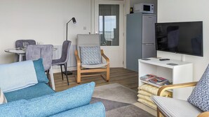Un salon moderne comprenant un canapé, des fauteuils, une table à manger, un téléviseur et un réfrigérateur.