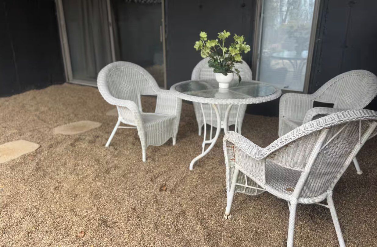 Un patio couvert aménagé avec des meubles en osier, une table en verre et une plante en pot.