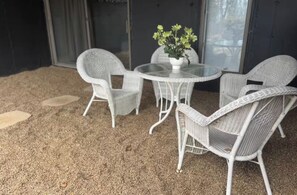 Un espacio cubierto con patio, mobiliario de mimbre, una mesa de vidrio y una planta en maceta.