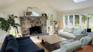 A living room with a stone fireplace, a sofa, a coffee table, and a view of the outdoors.