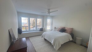 A bedroom with a bed, a window seat, a ceiling fan, and a view of the outdoors.