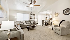 A living room with a sofa, coffee table, and armchair, a dining area with a table and chairs, and a kitchen in the background. - 2Min>RedhawkGolfCourse★LongStays★300mbps★1300ft²★ (Nampa)