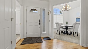 A hallway leading to a dining area with a round table and chairs, a door with a frosted glass panel, and a chandelier. - *Backyard*King*Parking*100Mbps*Smart TV*Bbq*W/D (Boise)