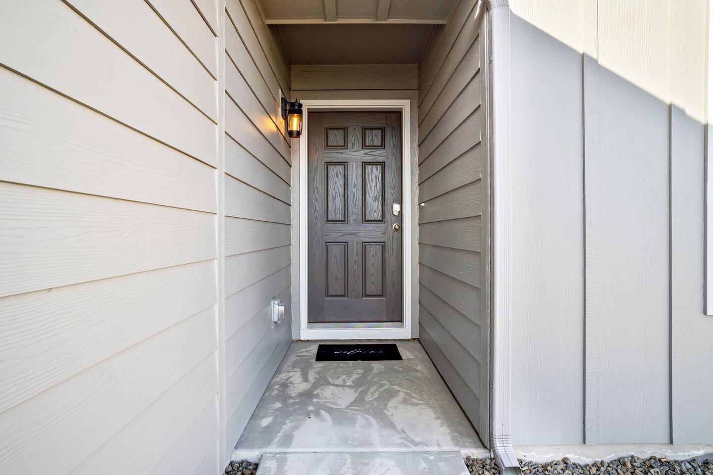 A narrow entrance with a dark wooden door, light siding, and a small step leading up to the door.