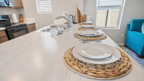 Een moderne keuken met een groot kookeiland, roestvrijstalen apparatuur en een blauwe bank op de achtergrond.